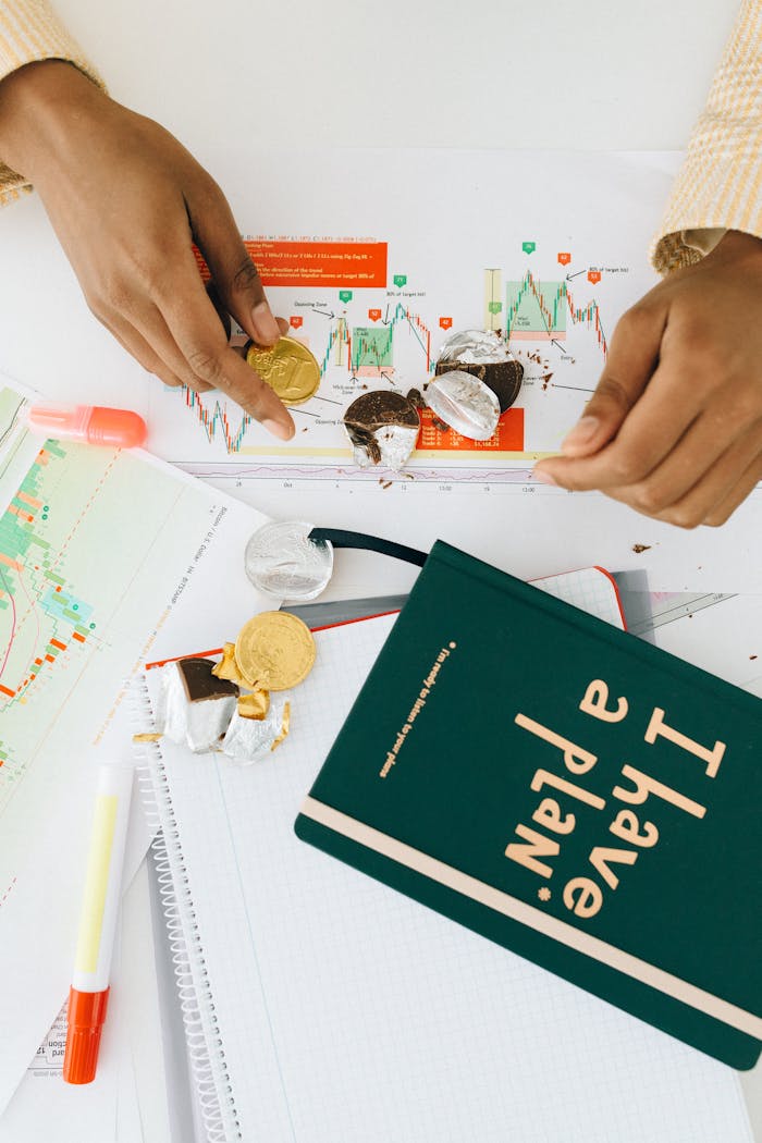 Hands arranging chocolate coins on financial documents and graphs, depicting business strategy.